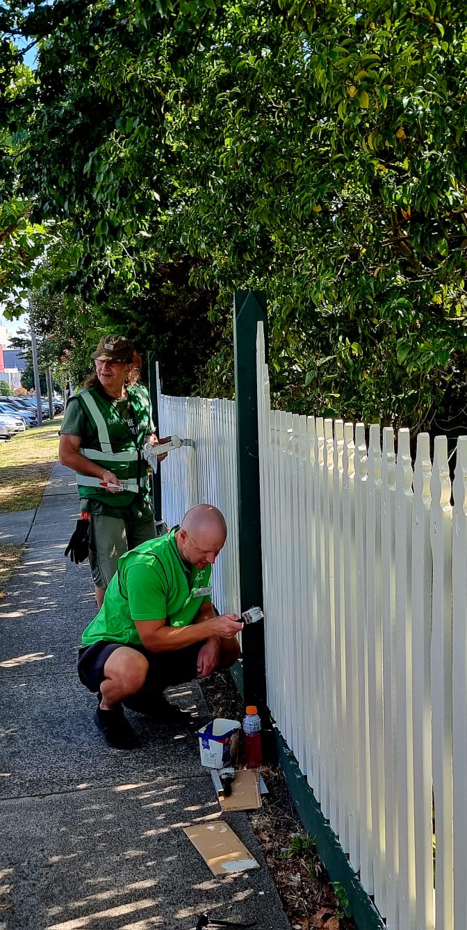 Two Brigade volunteers painting a community fence